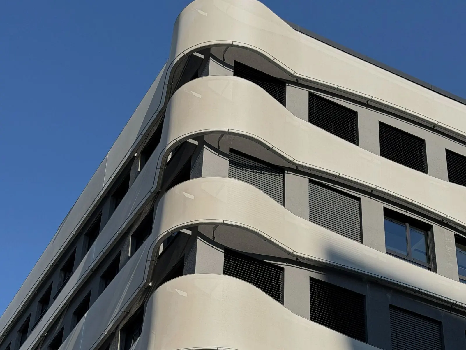 Moderne Wohnhausfassade mit geschwungenen Balkonbändern vor tiefblauem Himmel